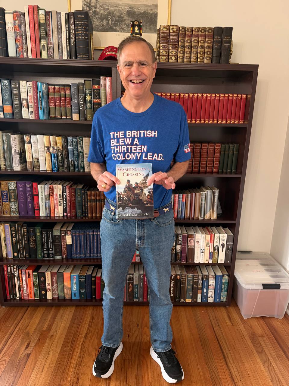 John Kuhn holding Washington's Crossing in front of his bookshelf